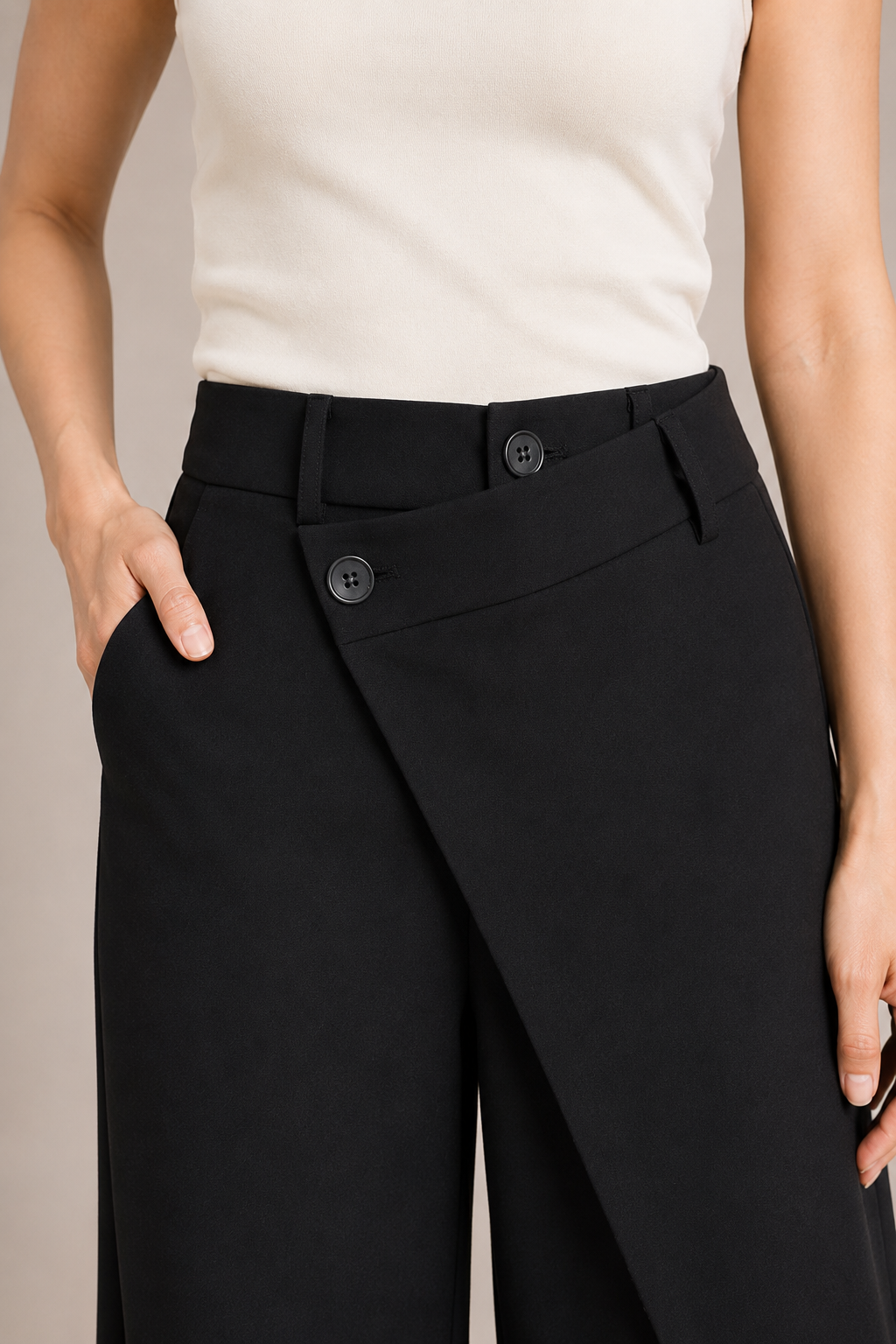 Close-up of the black trousers showing the layered asymmetric waistband, two-button closure and wrap-front construction