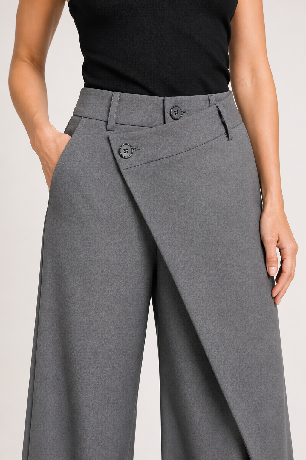 Close-up of the grey trousers showing the layered asymmetric waistband, two-button closure and wrap-front construction