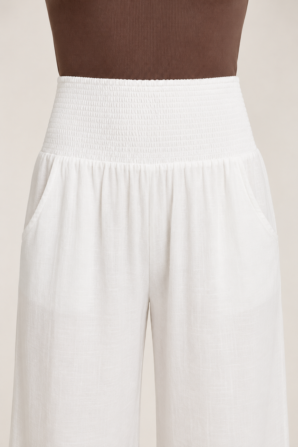 Close-up of the white palazzo trousers showing the broad smocked waistband, gathered join and side pockets